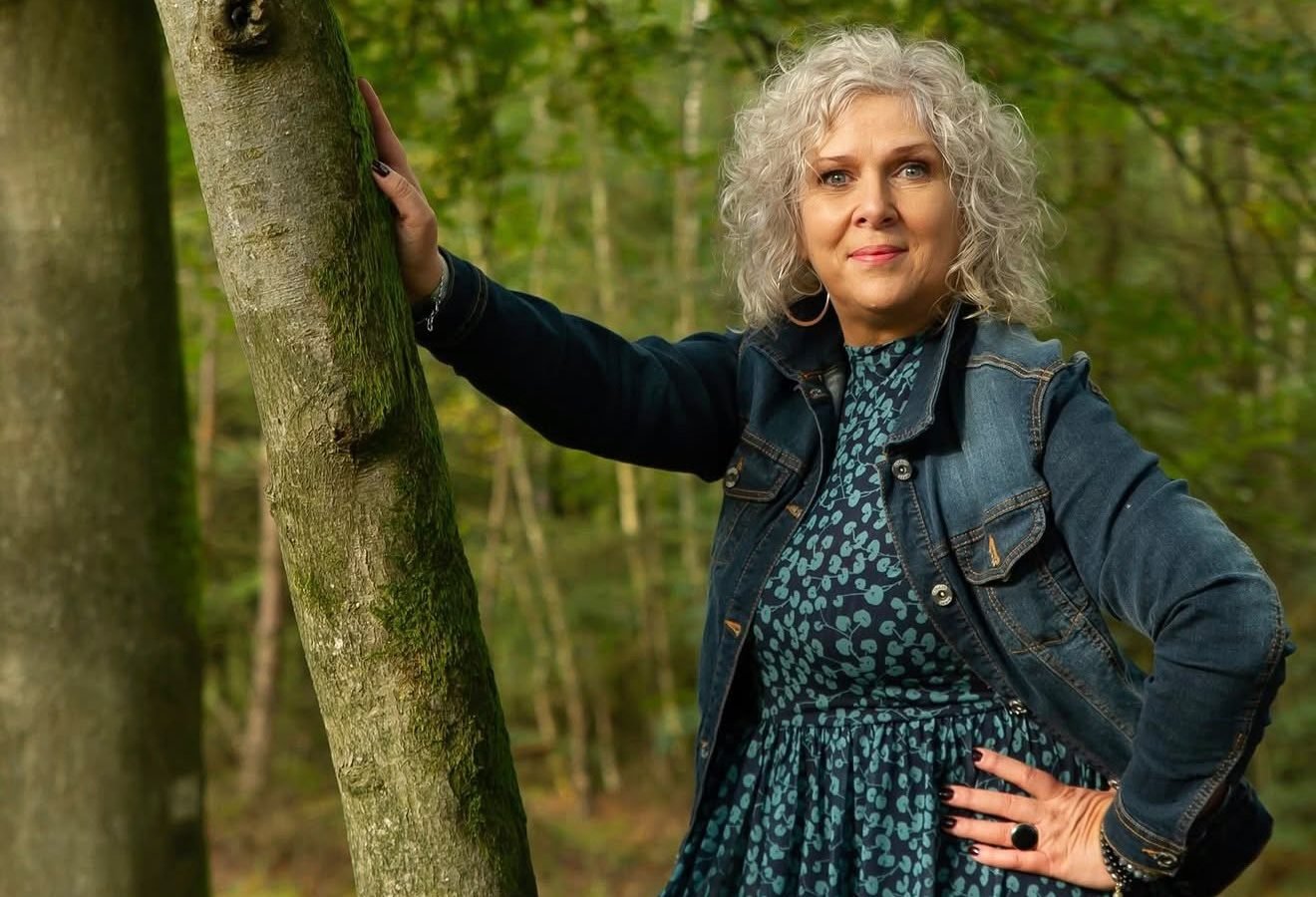 Will Hut-Doornik in het bos, met de hand op een boomstam