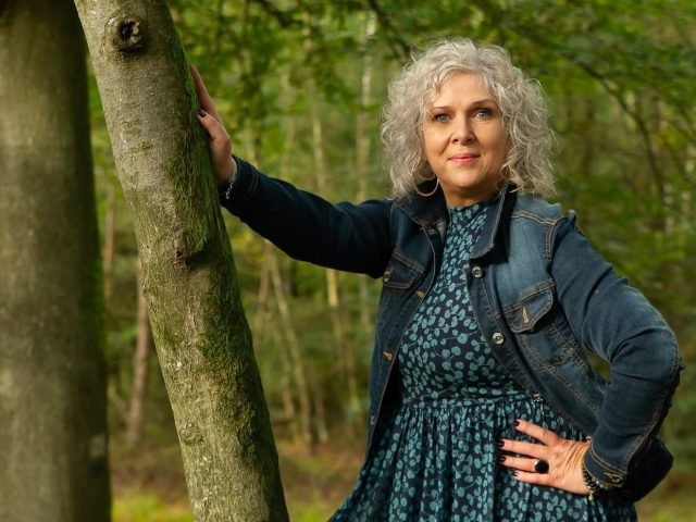 Will Hut-Doornik in het bos, met de hand op een boomstam
